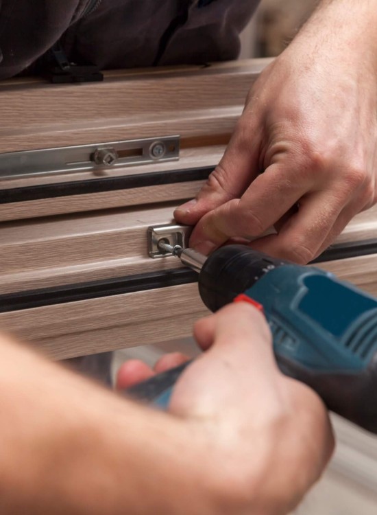 Handwerker befestigt mit einem Akkuschrauber eine Metallschiene am Holzrahmen eines Fensters.