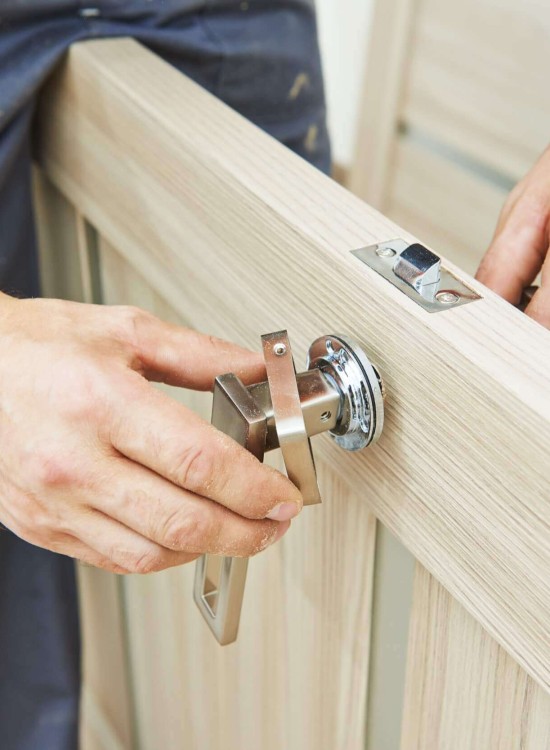 Handwerker montiert einen Türgriff an einer hellen Holztür und richtet das Schloss präzise aus.