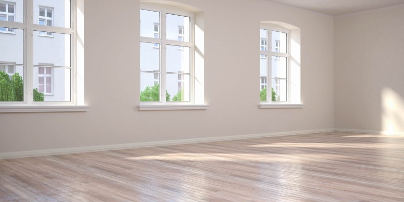 Heller leerer Raum mit drei großen Fenstern und frisch verlegtem Parkettboden.