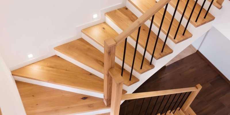 Moderne Holztreppe mit schwarzem Geländer und integrierter LED-Stufenbeleuchtung in einem hellen Treppenhaus.